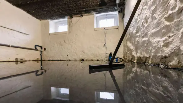 Flooded basement with standing water and a squeegee leaning on the wall